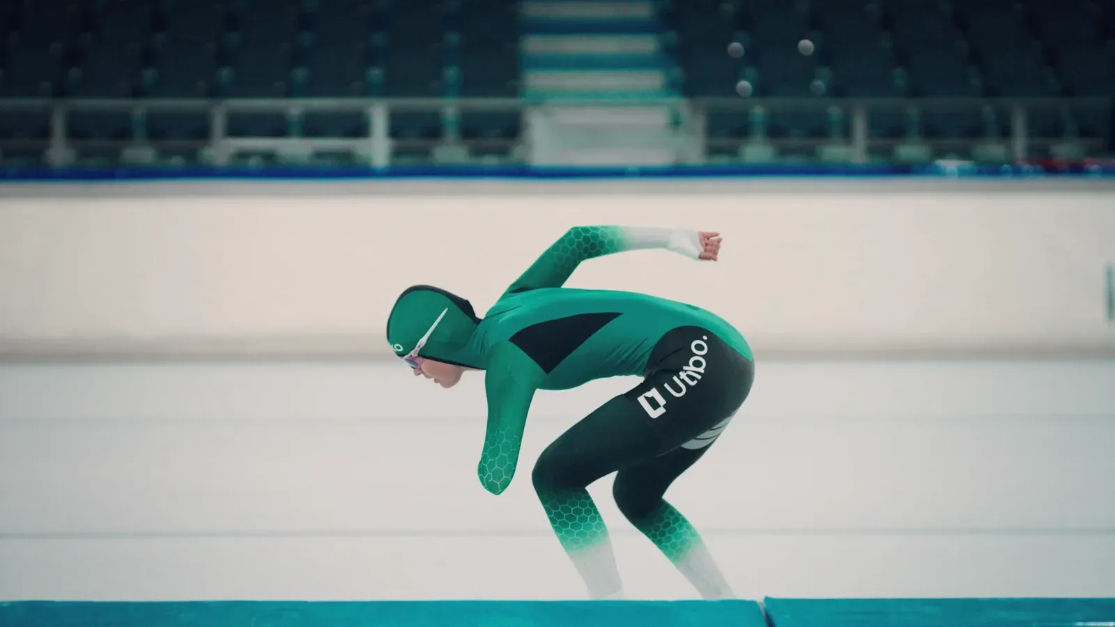 Een schaatser in de startpositie op het ijs, met Utibo op het pak